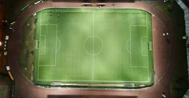 Top-down aerial view of a football stadium illuminated at night with minimal crowd.