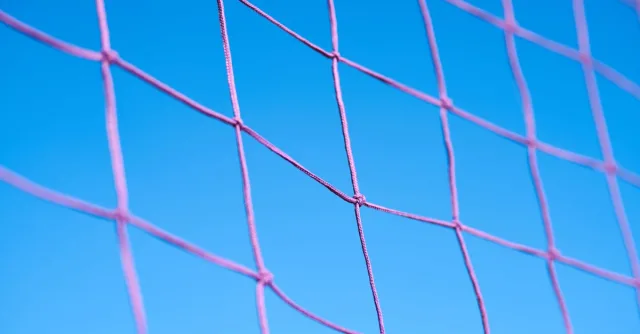 Close-up of a pink volleyball net pattern against a clear blue sky, showcasing geometric shapes.