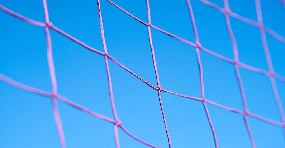 Close-up of a pink volleyball net pattern against a clear blue sky, showcasing geometric shapes.