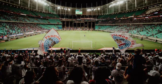 Energetic soccer fans cheer during a night match at a large stadium, creating an exciting atmosphere.