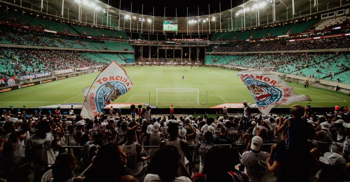 Energetic soccer fans cheer during a night match at a large stadium, creating an exciting atmosphere.
