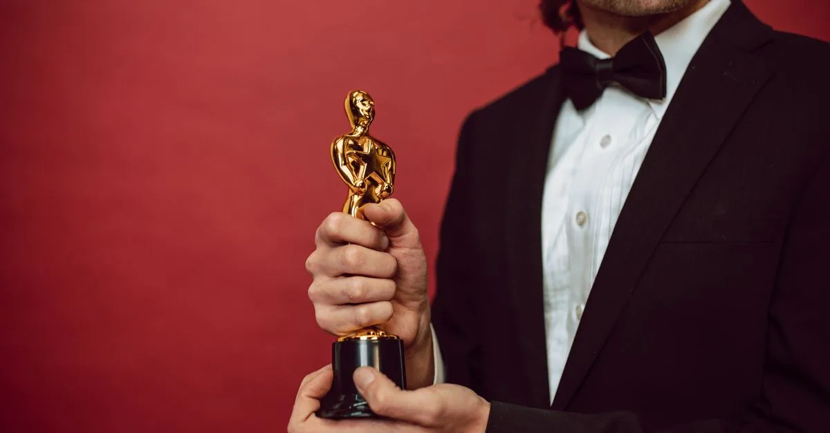 Elegant man in tuxedo holding a gold trophy against a red background, celebrating an achievement.