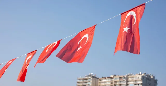 Turkish national flags fluttering in the wind with a cityscape in the background, showcasing national pride.