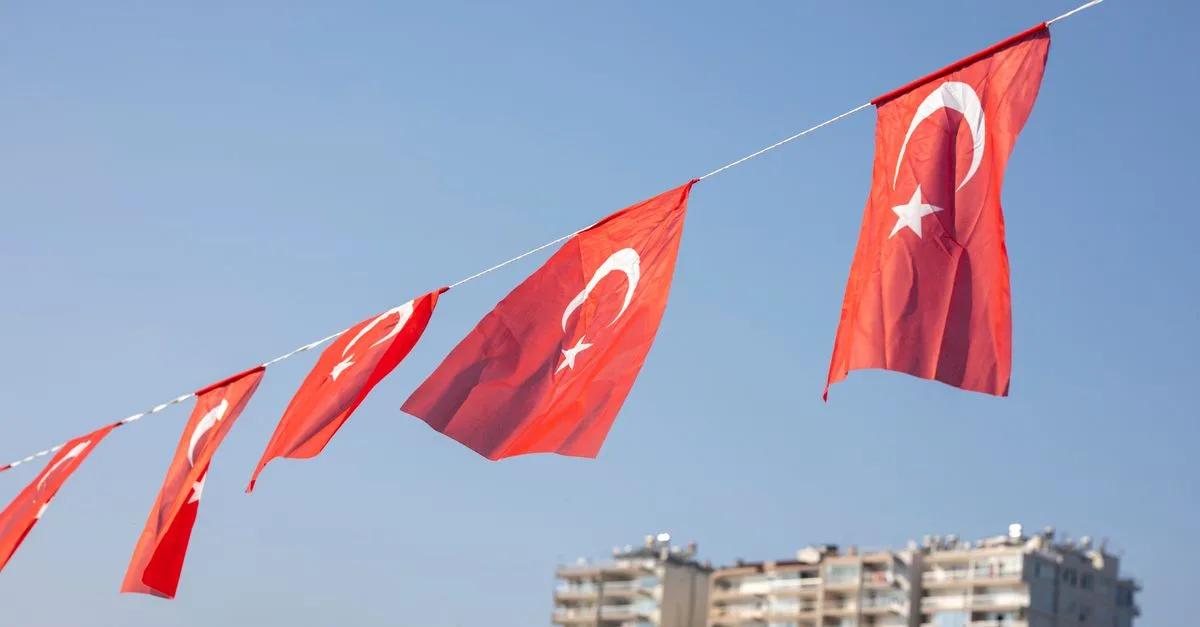Turkish national flags fluttering in the wind with a cityscape in the background, showcasing national pride.