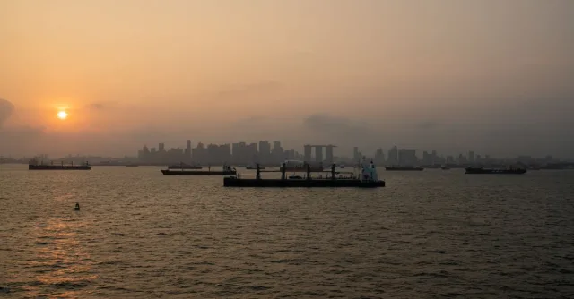 Serene sunset view over Singapore Harbor with ships silhouetted against the skyline.