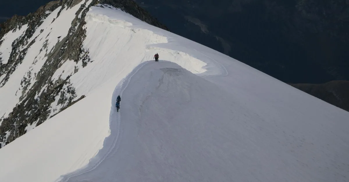 Two climbers ascend a snow-covered mountain ridge, showcasing adventure in a winter landscape.