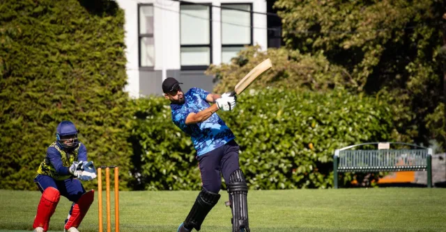 Cricketer hitting the ball with wicketkeeper ready during an outdoor cricket match.