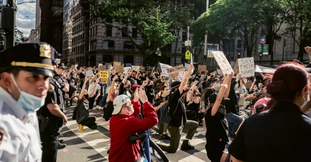 A group of protesters kneeling on a city street holding signs for Black Lives Matter, advocating justice and equality.