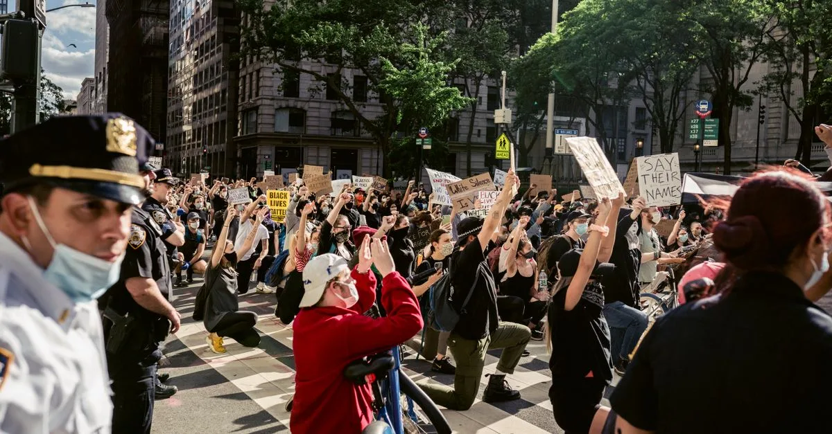 A group of protesters kneeling on a city street holding signs for Black Lives Matter, advocating justice and equality.