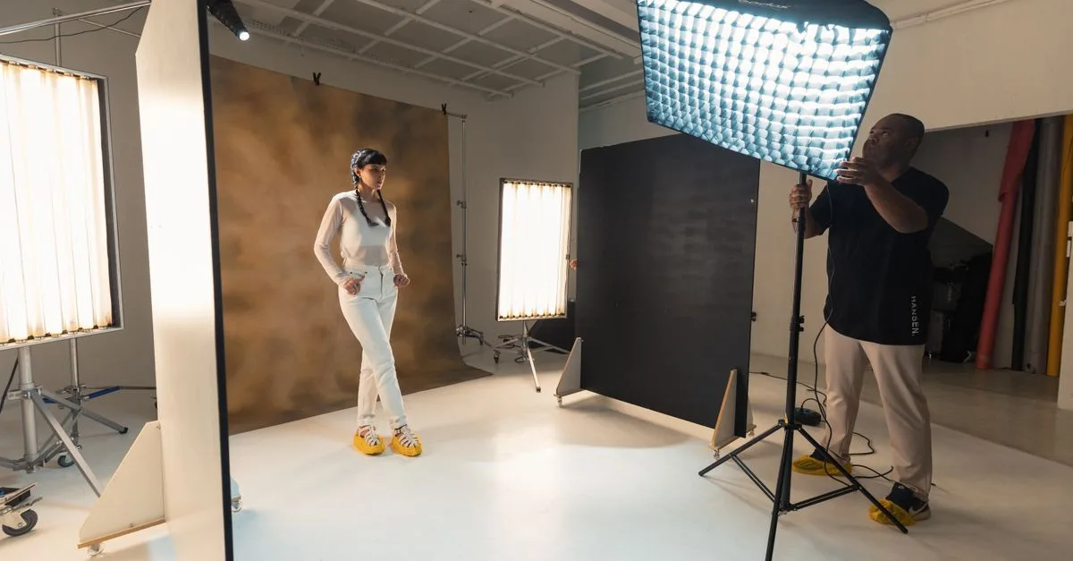 Photographer adjusts lighting for a model in a professional indoor studio setting.