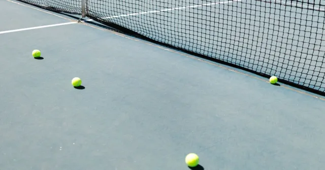 A tennis court featuring a net and several tennis balls lying on the ground, well-lit by sunlight.
