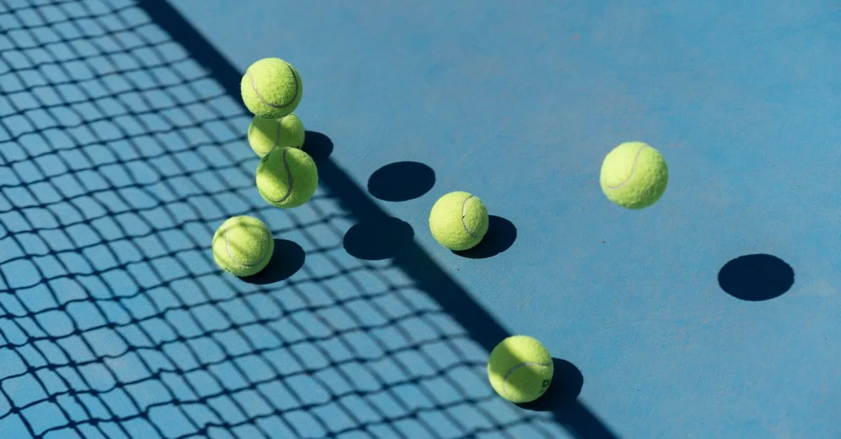 Tennis balls scattered on a blue court casting shadows, captured from above for a high-energy sports vibe.