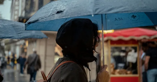 Side view of a woman holding an umbrella, standing in a rainy street, capturing a moment in urban life.