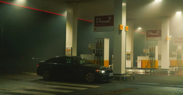 A BMW sports car parked at a Shell gas station at night, featuring bright lights and an urban setting.