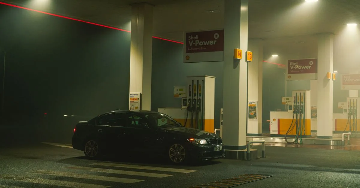 A BMW sports car parked at a Shell gas station at night, featuring bright lights and an urban setting.