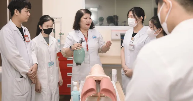 Group of medical students practicing skills with a training mannequin in a classroom setting.