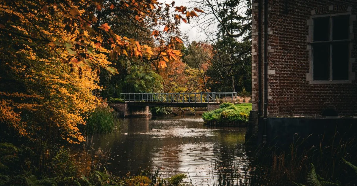 Tranquil autumn scene featuring a bridge and brick building by a stream in Malle, Belgium.