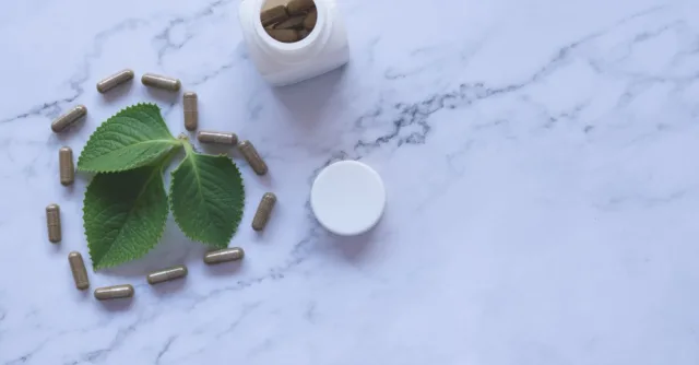 Flat lay of herbal capsules, leaves, and bottle on marble surface, symbolizing natural wellness.