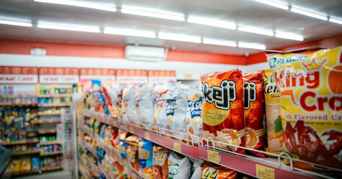Wide shot of vibrant snack aisle in a supermarket with various chip bags on display.