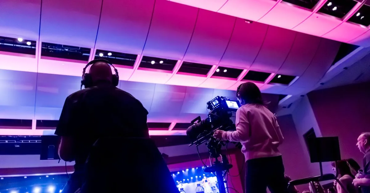 Professional camera crew filming a live event indoors, capturing vibrant stage lighting.
