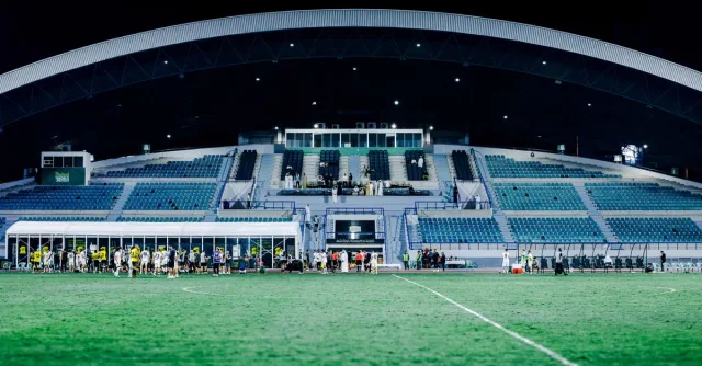 Panoramic view of a modern stadium during a night football match, vibrant and well-lit atmosphere.