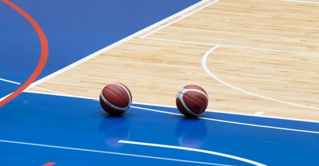 Two basketballs resting on a blue indoor basketball court with wooden flooring.