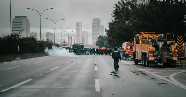 Tense urban scene showing police presence in riot gear amidst smoke during a protest.