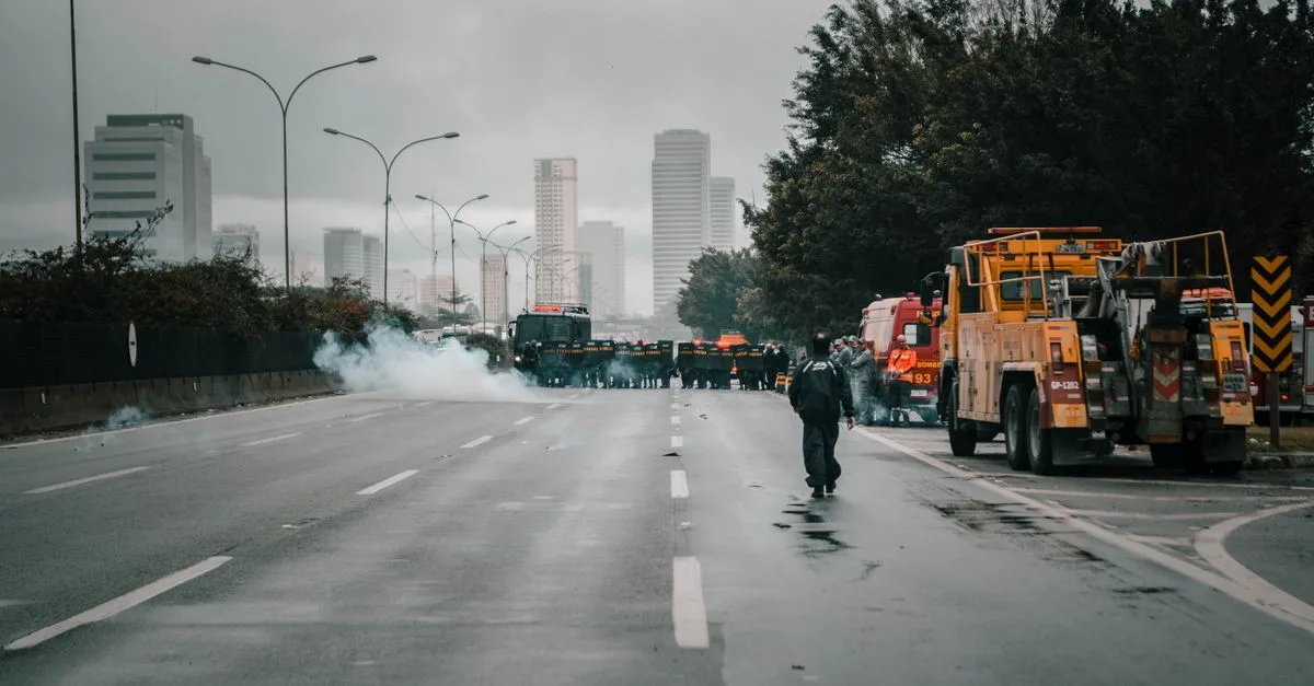 Tense urban scene showing police presence in riot gear amidst smoke during a protest.