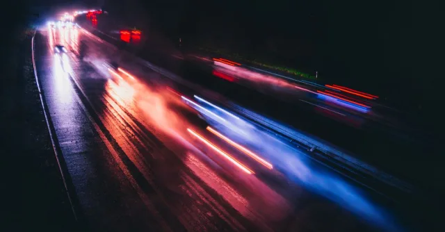Long exposure photo capturing vibrant light trails on a rainy highway night.