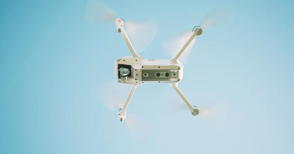 A sleek white drone flying under a clear blue sky, capturing aerial views.