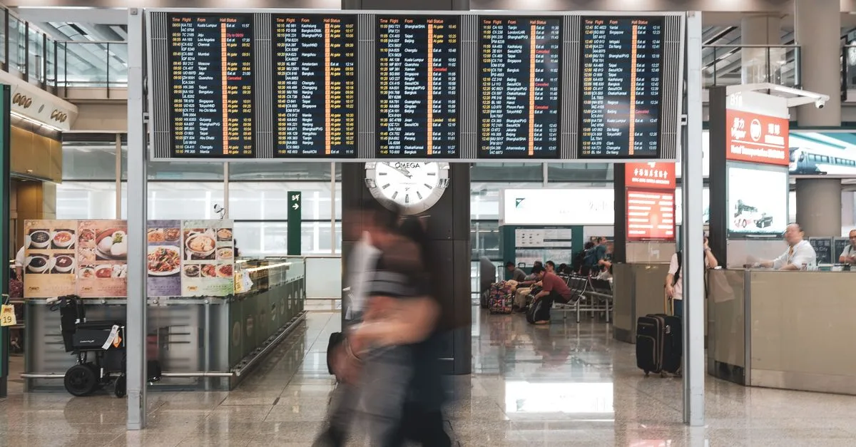 Blurred motion of travelers in a modern airport terminal with departure screens and a prominent clock.