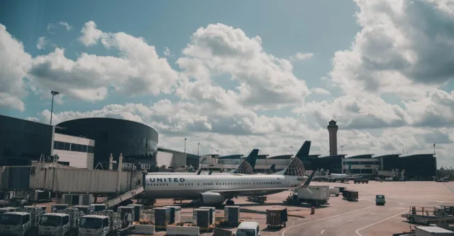 A United airplane parked on the airport apron under a scenic cloudy sky.