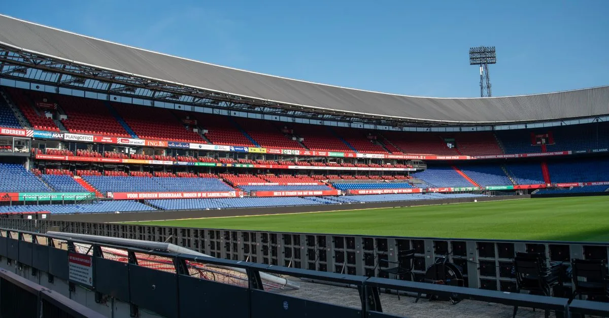 Panoramic view of De Kuip stadium in Rotterdam with empty stands and a clear blue sky.