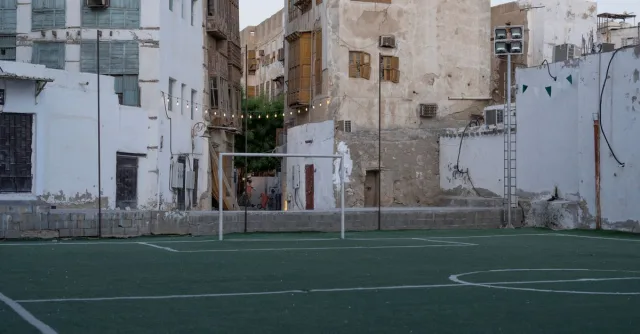 An empty soccer field in the heart of Jeddah's historic district, surrounded by traditional architecture.