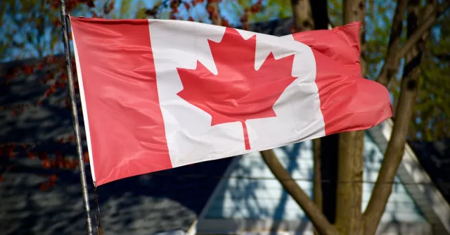 A vibrant Canadian flag, featuring the iconic maple leaf, waves outdoors in a sunny setting.