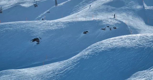 Scenic view of a snowy ski resort slope with skiers and chairlifts under a clear winter sky.
