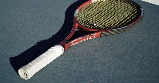 A high-quality tennis racket placed on a blue tennis court under sunlight.