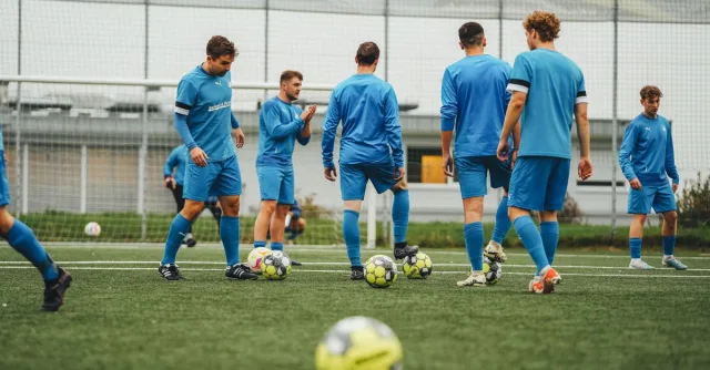 A group of soccer players in blue uniforms training outdoors on a grass field.