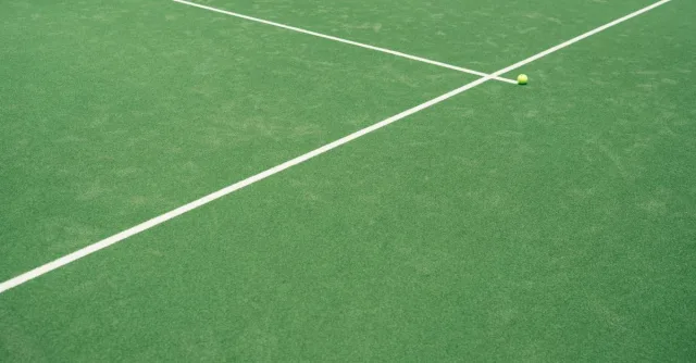 A tennis ball on a green court displaying crisp white lines under daylight.