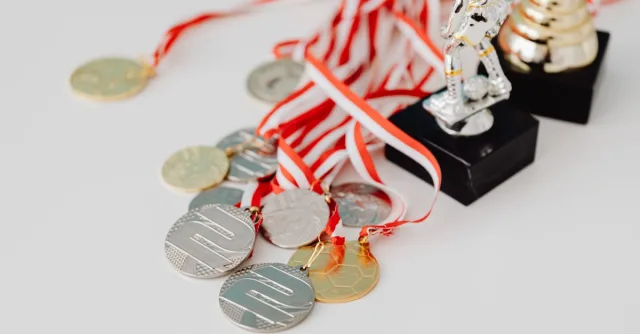 A varied collection of silver and gold medals alongside trophies on a white surface, showcasing achievement.