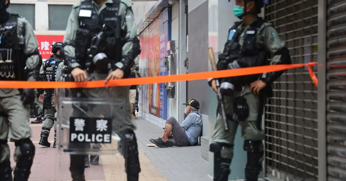 Urban environment with police presence and a civilian sitting against a wall, showing tension.