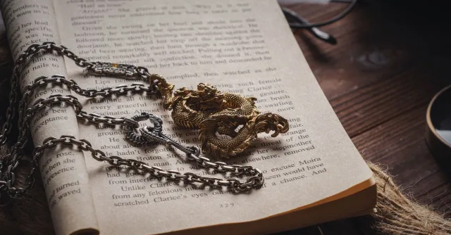 An intricate dragon necklace with chain on an open book, creating a vintage and artistic look.