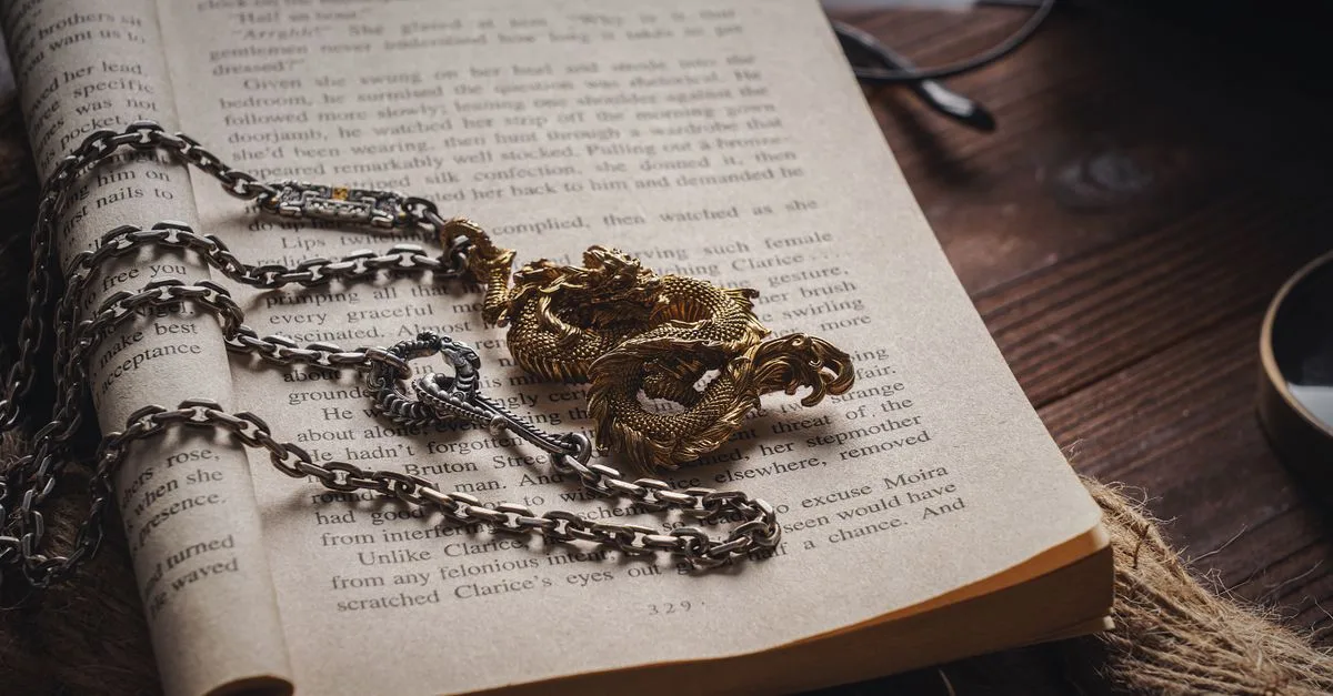 An intricate dragon necklace with chain on an open book, creating a vintage and artistic look.