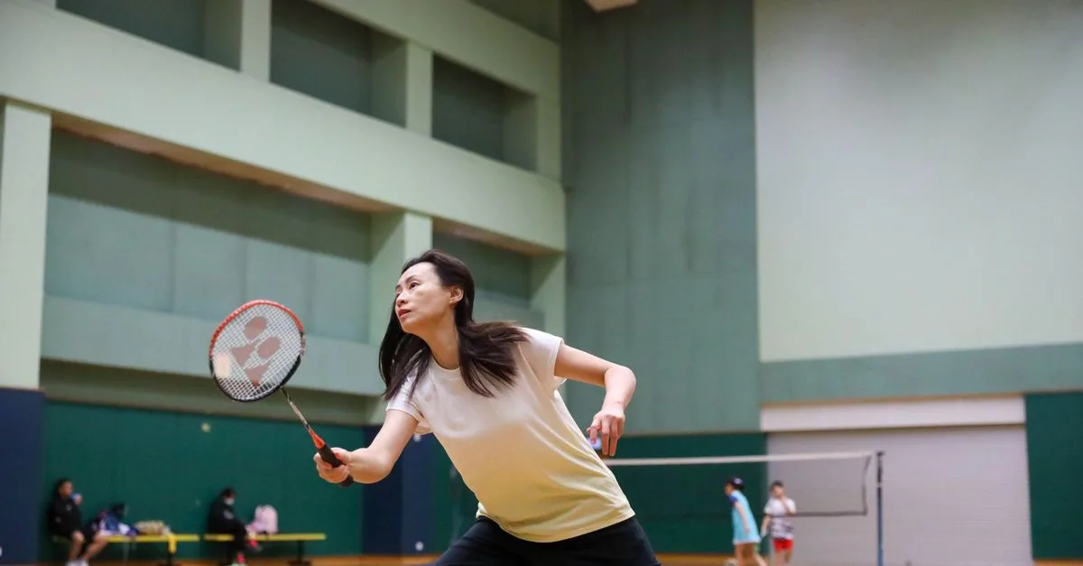 A female athlete playing badminton indoors, focused intently on the game.