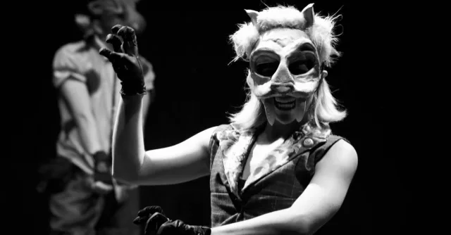 A captivating black and white image of actors in animal masks performing on stage, creating an eerie atmosphere.