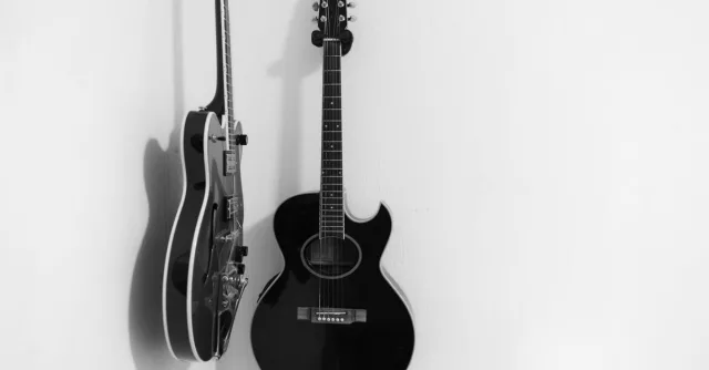 A sleek black acoustic guitar and an elegant electric guitar hang stylishly on a white wall, showcasing musical instruments.
