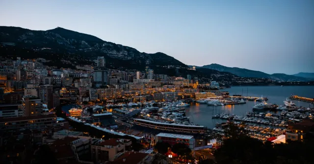 Twilight view of Monaco's harbor with yachts and city lights by the Mediterranean Sea.
