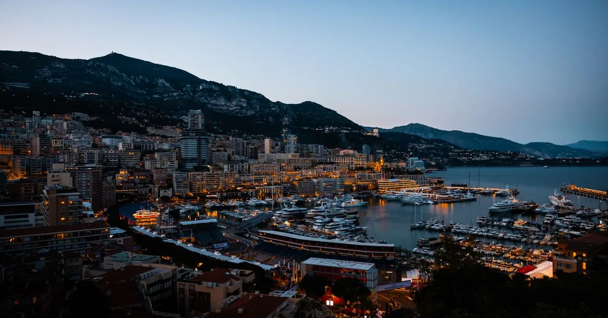 Twilight view of Monaco's harbor with yachts and city lights by the Mediterranean Sea.