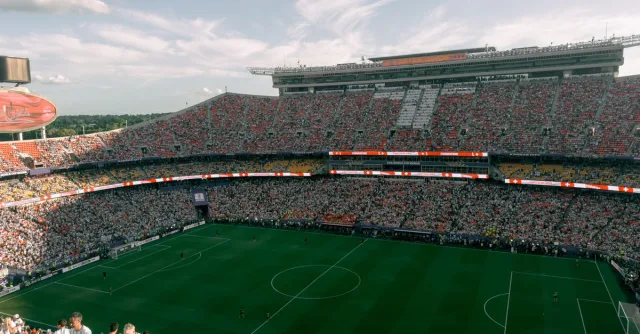 Aerial view of a lively soccer match in a bustling outdoor stadium filled with enthusiastic fans.