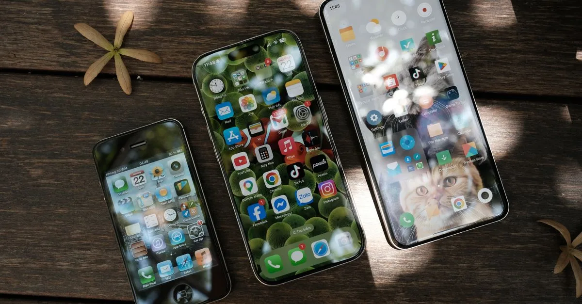 A collection of smartphones showing different app icons, placed on a wooden surface in natural light.